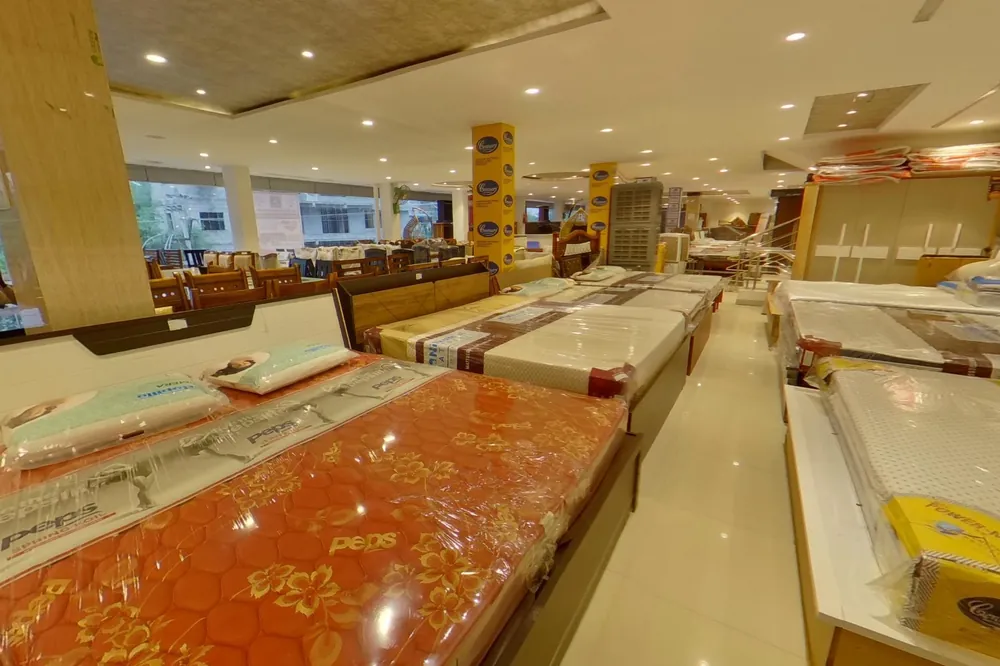 Wide showroom aisle with multiple mattresses on display in protective packaging, Century brand stands visible, dining furniture in background